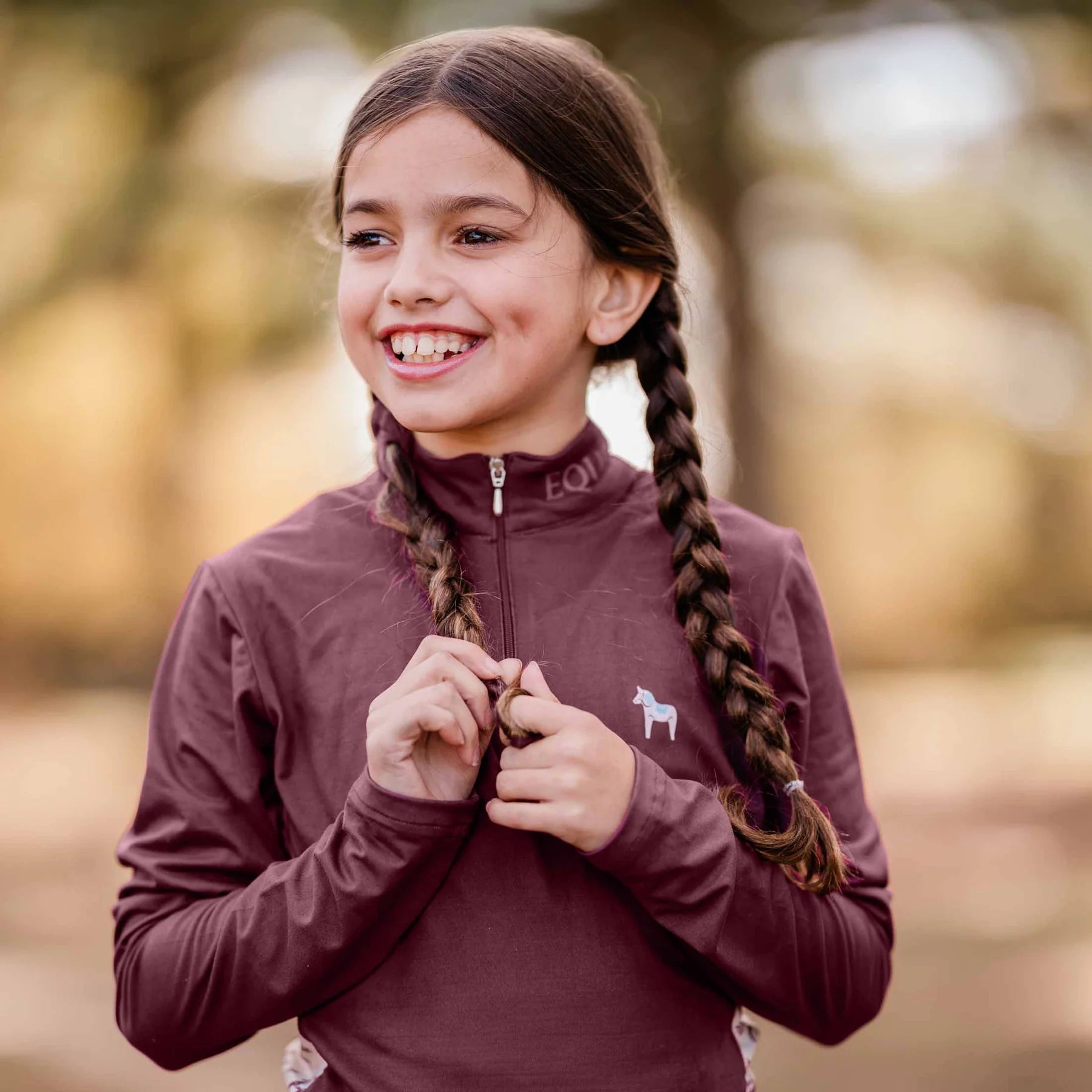 Front closeup view of a young model wearing the Burgundy Equinavia Lena Kids Long Sleeve Quarter Zip outdoors