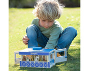 Front view of a young male model playing with the Breyer Breyer Farms Wood Carry Stable outside