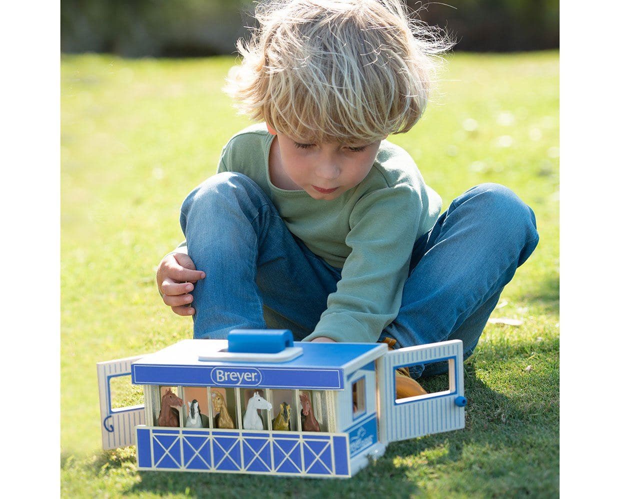 Front view of a young male model playing with the Breyer Breyer Farms Wood Carry Stable outside