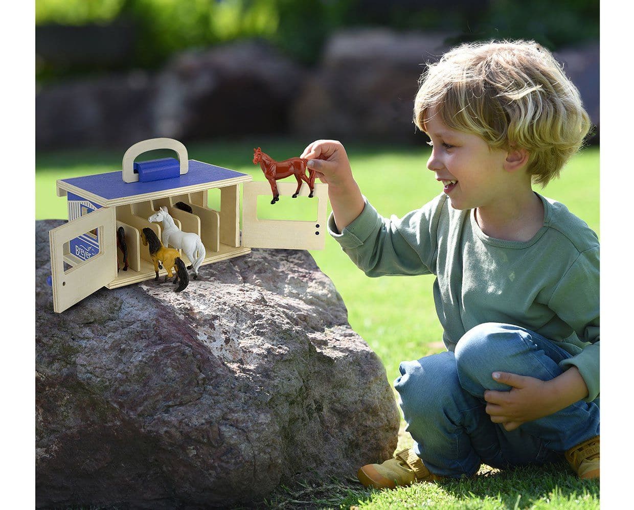 View of a young male model playing the with Breyer Breyer Farms Wood Carry Stable outside