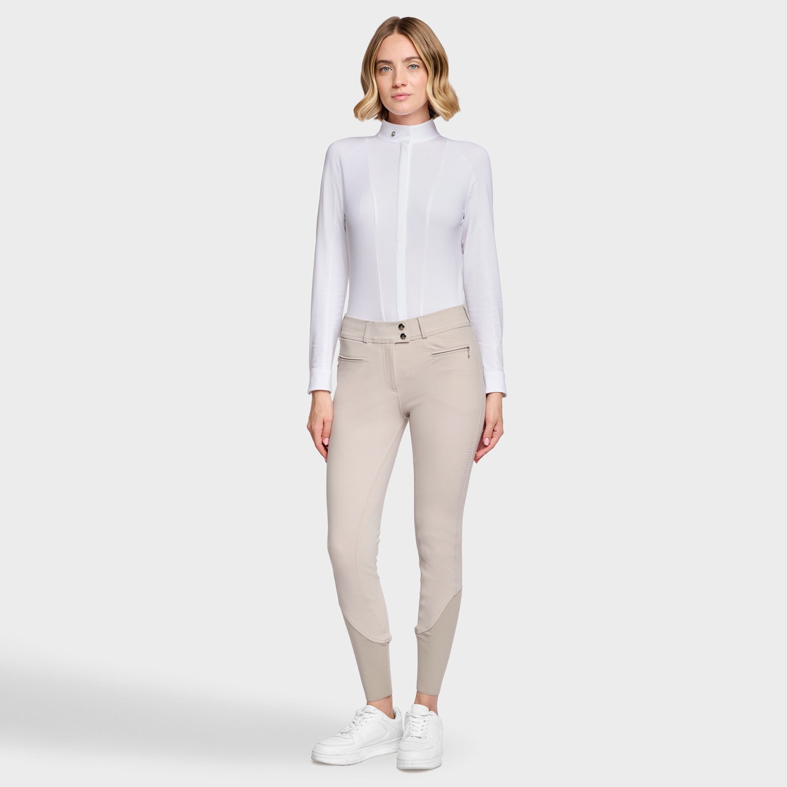Full body front view of a female model wearing the Beige Samshield Chloe 3D Knee Grip Breeches with a white shirt on a plain background