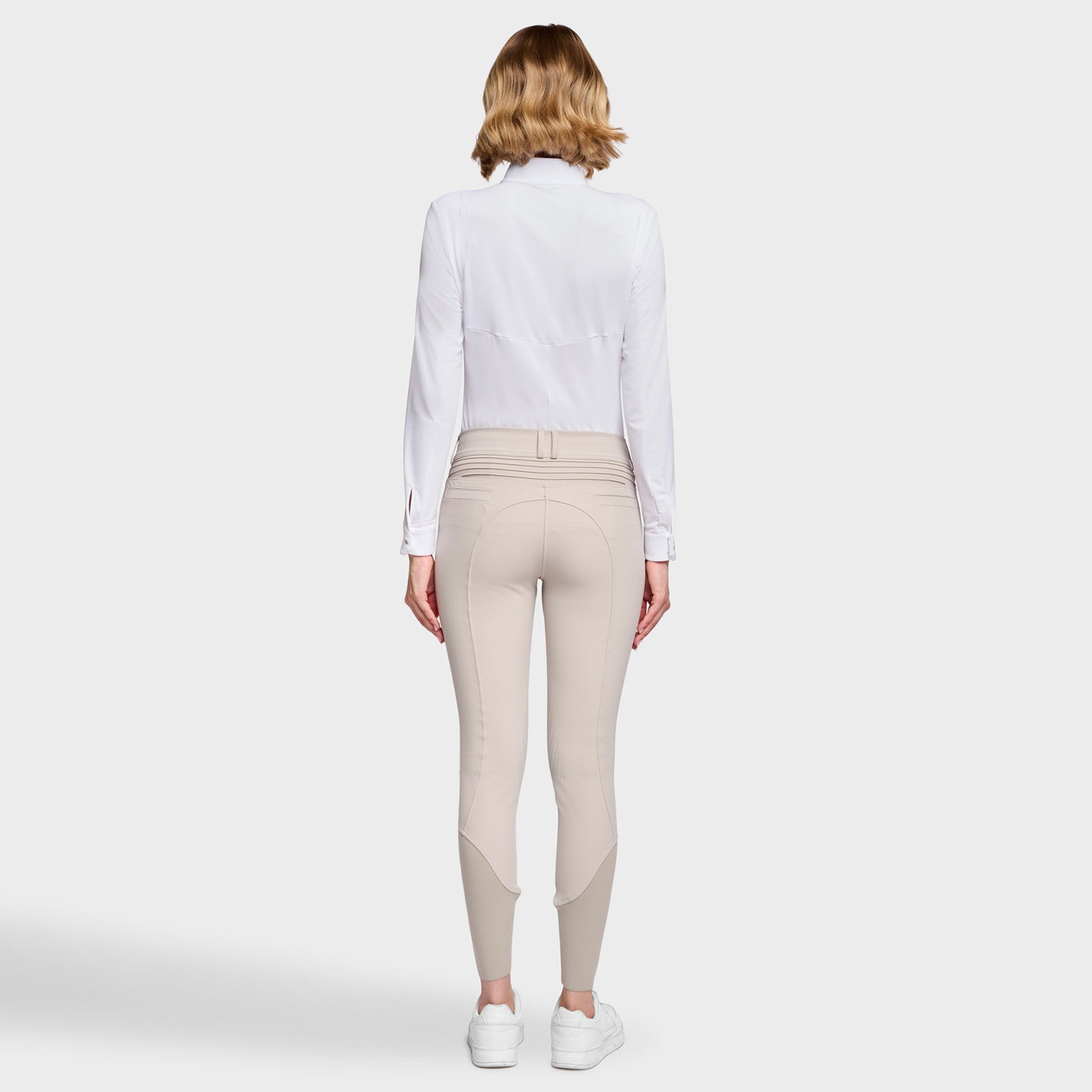 Full body back view of a female model wearing the Beige Samshield Chloe 3D Knee Grip Breeches with a white shirt on a plain background