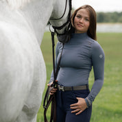 Front view of a female model wearing the Denim TKEQ Chloe High Collar Technical Top while facing a gray horse outside
