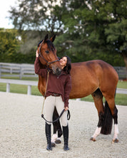 Front view of a female model wearing the Mocha Criniere Claire Sweater while standing next to a horse in an outdoor arena