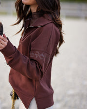Side view of a female model wearing the Mocha Criniere Claire Sweater while standing next to a horse in an outdoor arena