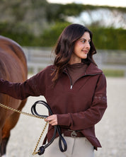 Front view of a female model wearing the Mocha Criniere Claire Sweater while standing next to a horse in an outdoor arena