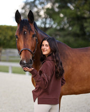 Back view of a female model wearing the Mocha Criniere Claire Sweater while standing next to a horse in an outdoor arena