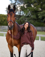 Front view of a female model wearing the Mocha Criniere Claire Sweater while standing next to a horse in an outdoor arena