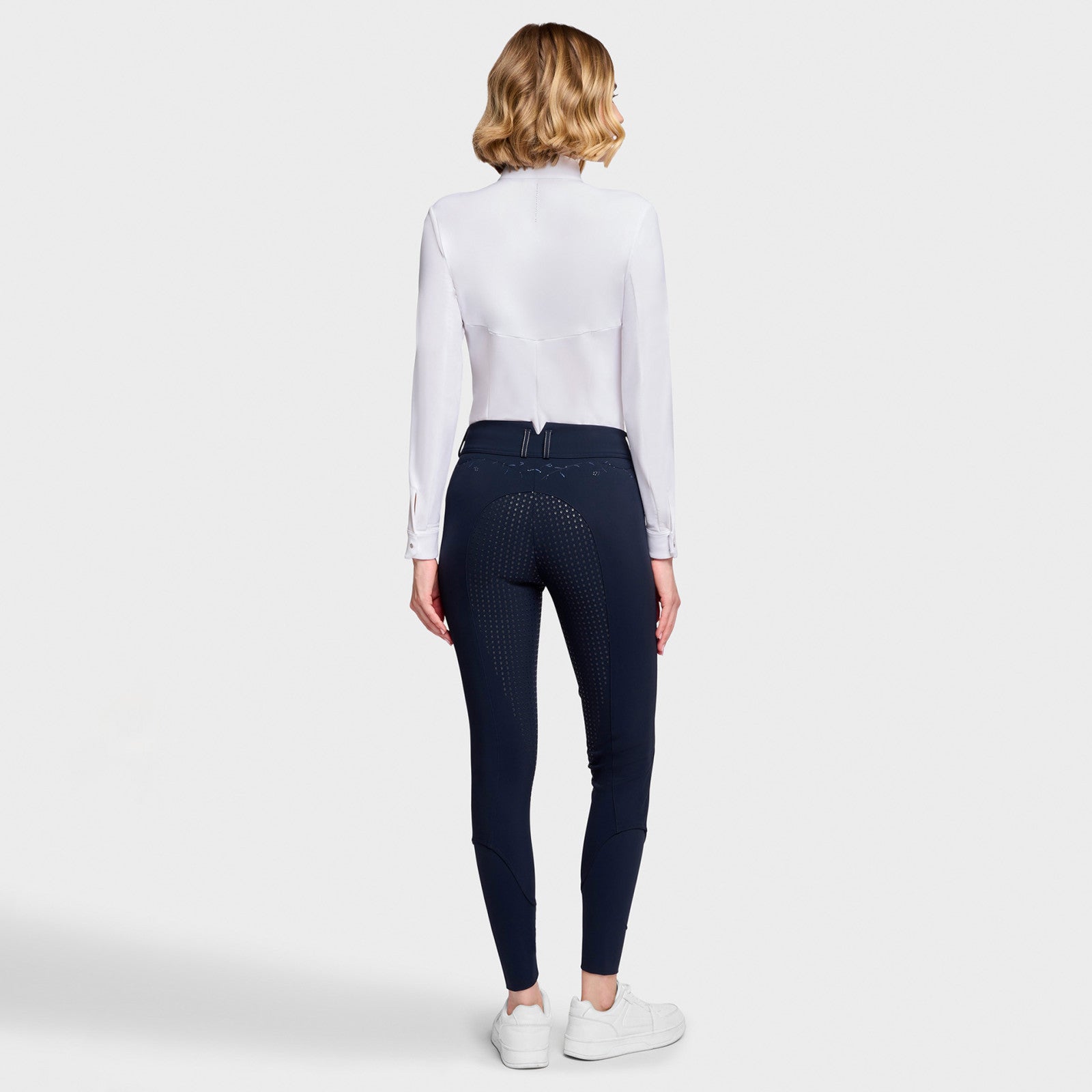 Full body back view of a female model wearing the Navy Samshield Delice Floral Full Grip Breeches with white shirt on a plain background