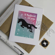 Front view of the I Believe In You Hunt Seat Paper Co. Greeting Card with its envelope and charm