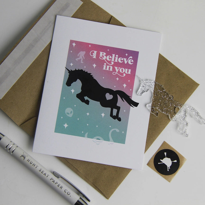 Front view of the I Believe In You Hunt Seat Paper Co. Greeting Card with its envelope and charm