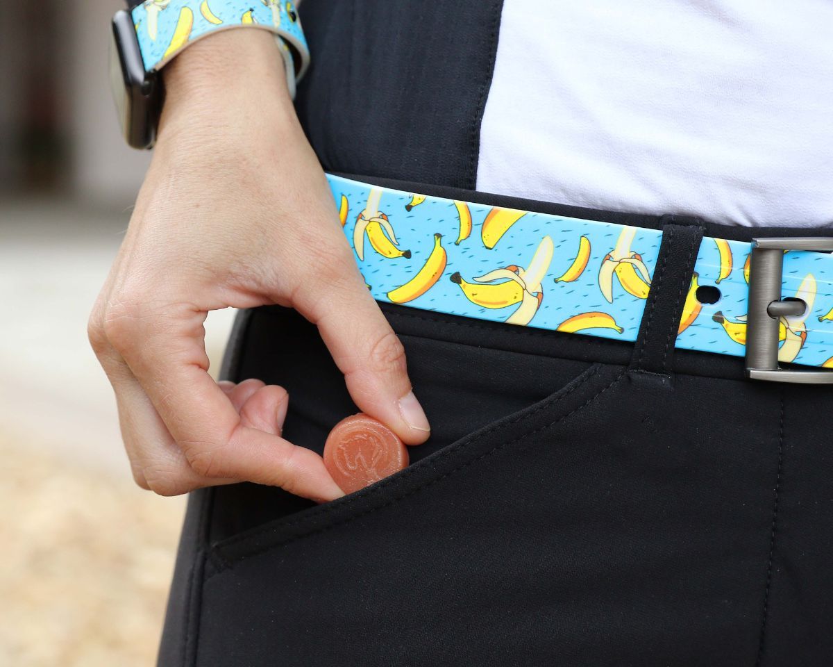 View of a model putting a Equine Elixirs Electrobites Gummie in her breeches pocket while she is wearing a banana design belt