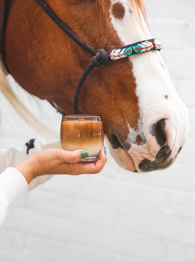 Front view of the Tack Room Stable Style Soy Wax Candle being held by a model's hand in front of a horse