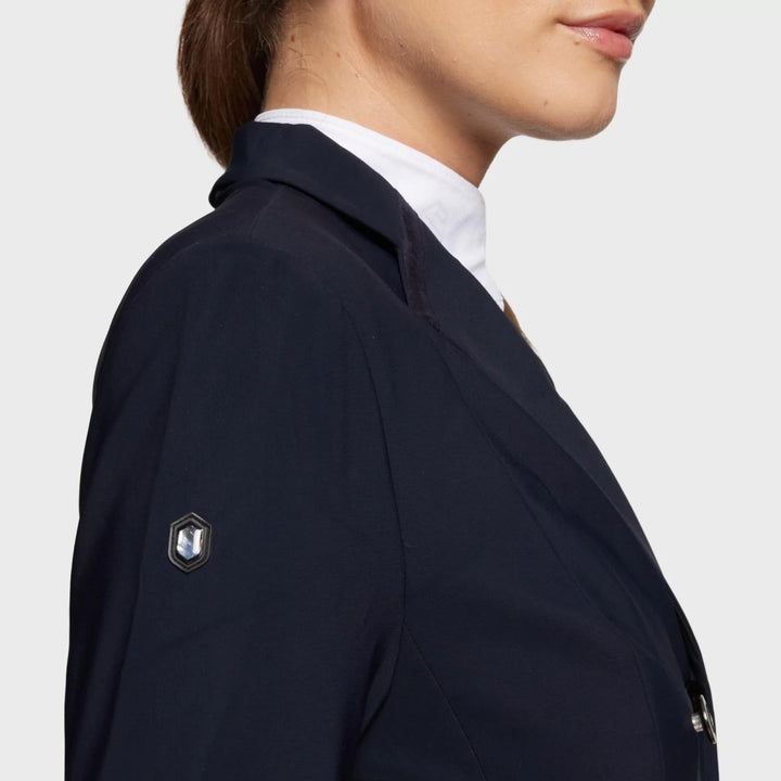 Close-up view of the logo on the Navy Samshield Alcantara Long Frac as worn by a female model on a plain background