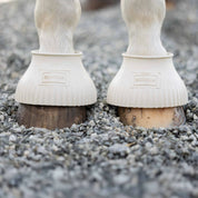 Front closeup view of a horse wearing the White Equinavia Rubber Pull On Bell Boots on small gravel