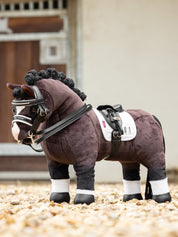 Side view of a bay toy pony wearing the LeMieux Toy Pony Dressage Saddle and Girth while standing on a gravel path