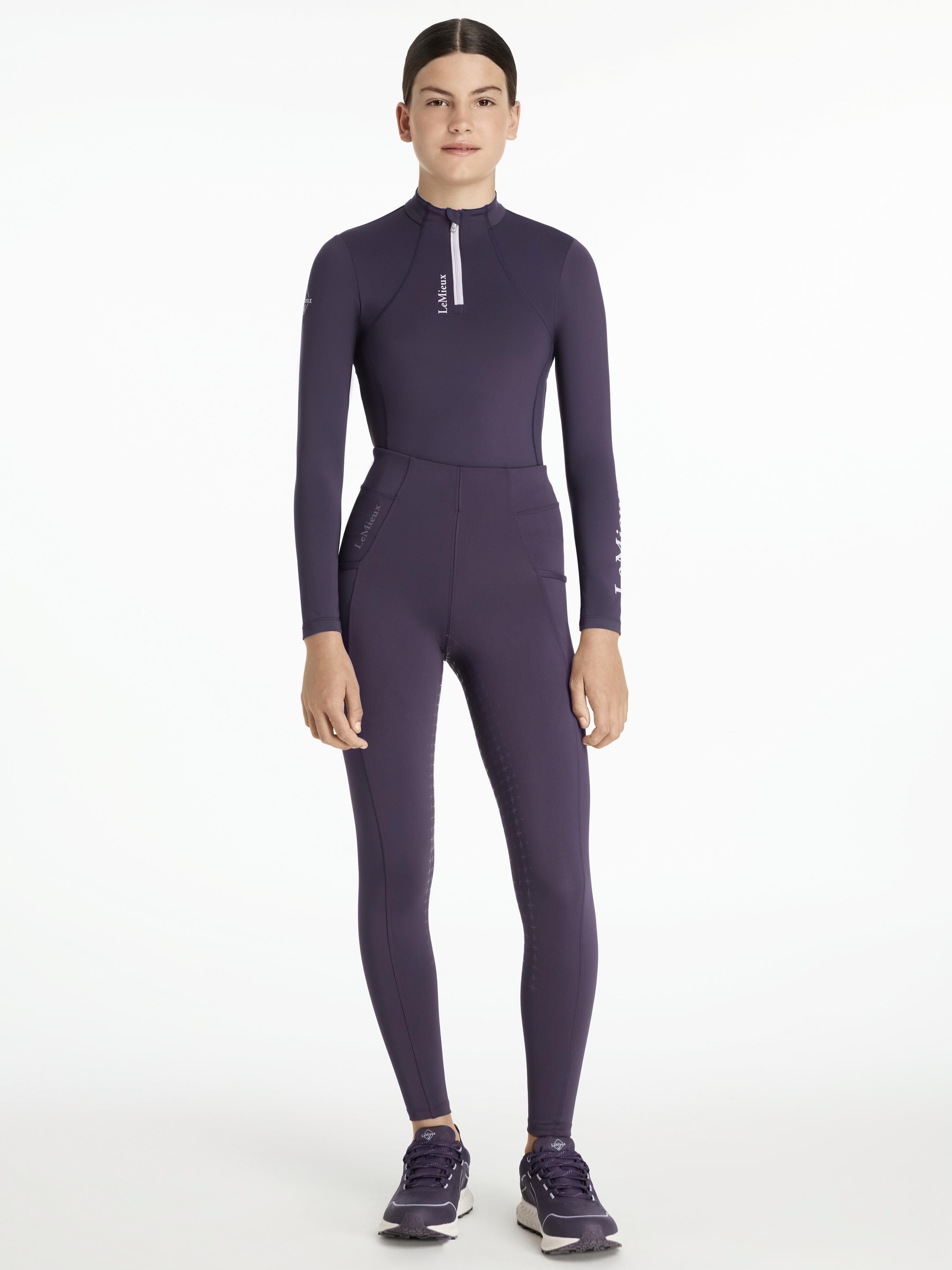 Full body front view of a young female model wearing the purple Lemieux Young Rider Orla Pull On Tight with coordinating purple top on a white background
