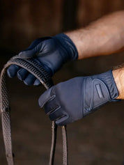 Person wearing dark blue gloves holding a horse bridle against a blurred background