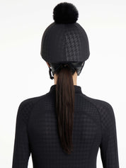 Back view of a female model wearing the Black Houndstooth LeMieux Aspen Hat Silk over a helmet on a plain background