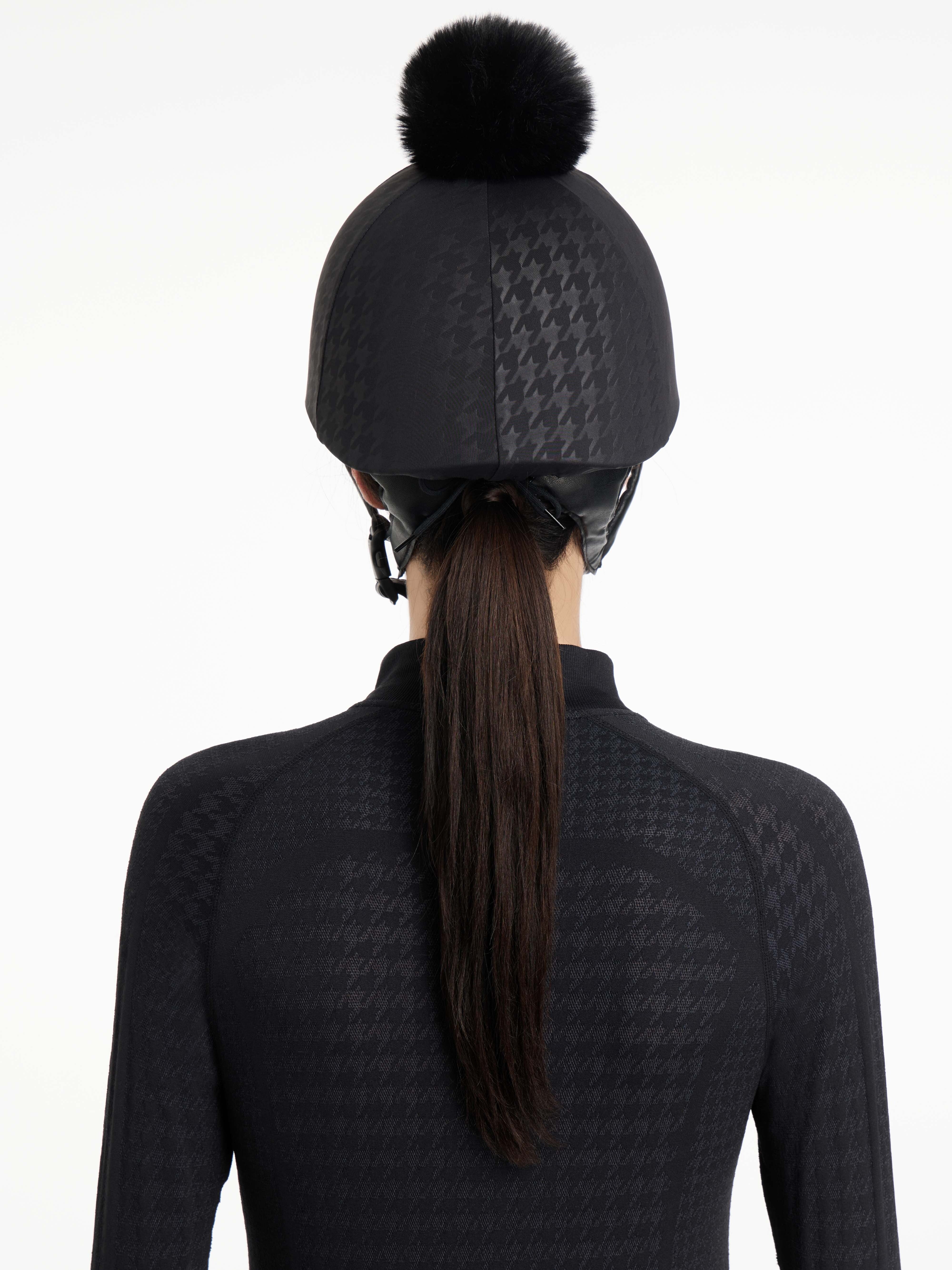 Back view of a female model wearing the Black Houndstooth LeMieux Aspen Hat Silk over a helmet on a plain background