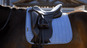 Close-up side view of a dark colored horse wearing the powder blue LeMieux Suede Dressage Square Pad