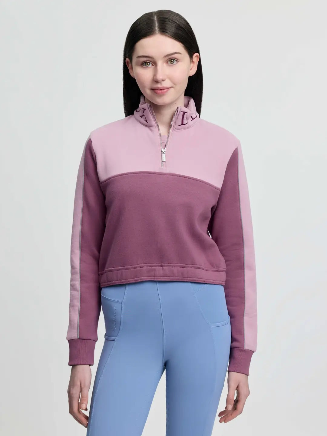 Front view of a young female model wearing the pink LeMieux Young Rider Cropped Kate Quarter Zip on a plain background