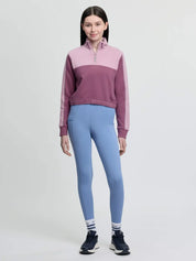 Full body front view of a young female model wearing the pink LeMieux Young Rider Cropped Kate Quarter Zip and blue tights on a plain background