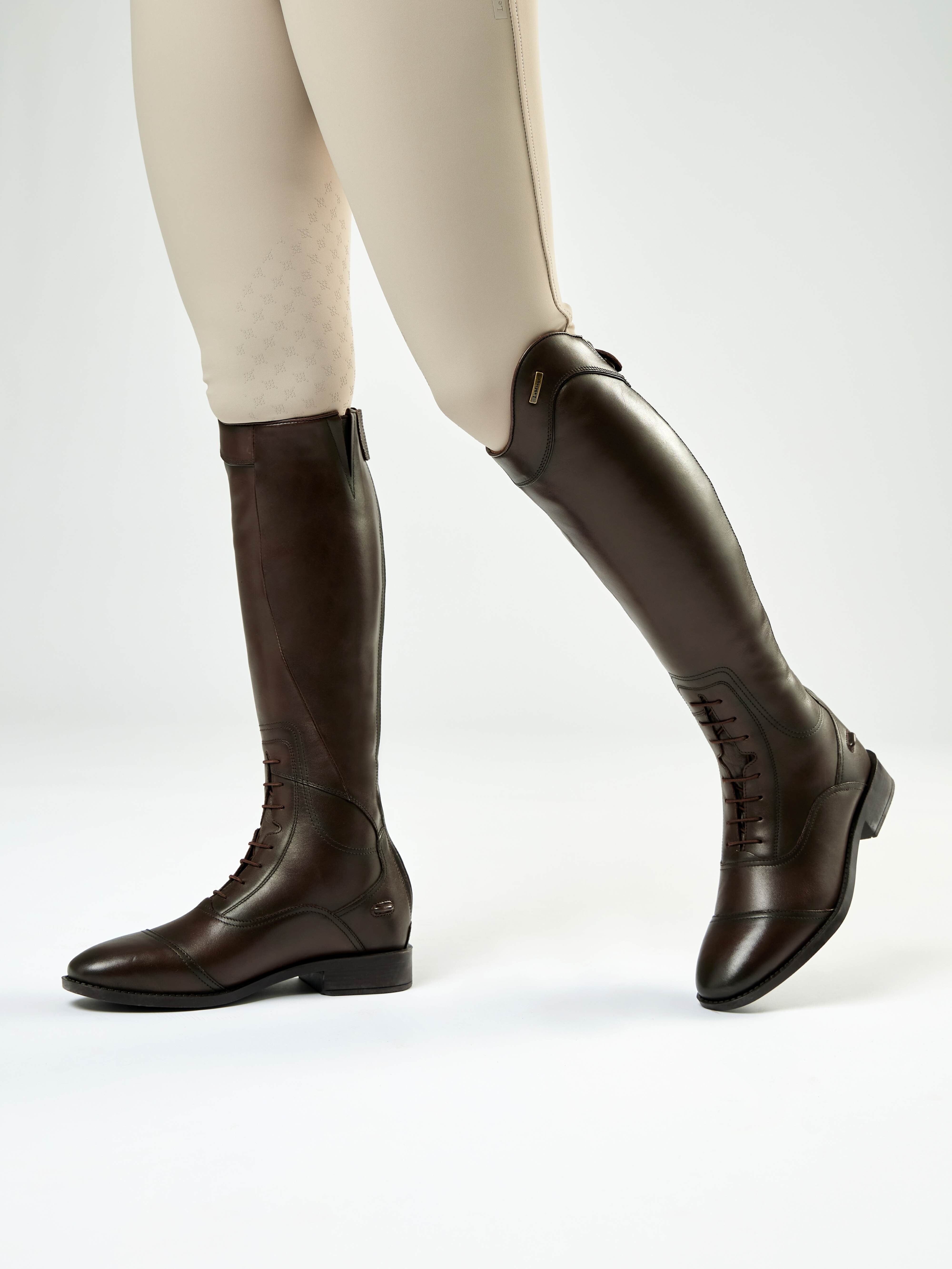 Side view of a model wearing a brown pair of LeMieux Junior Field Riding Boots on a plain background