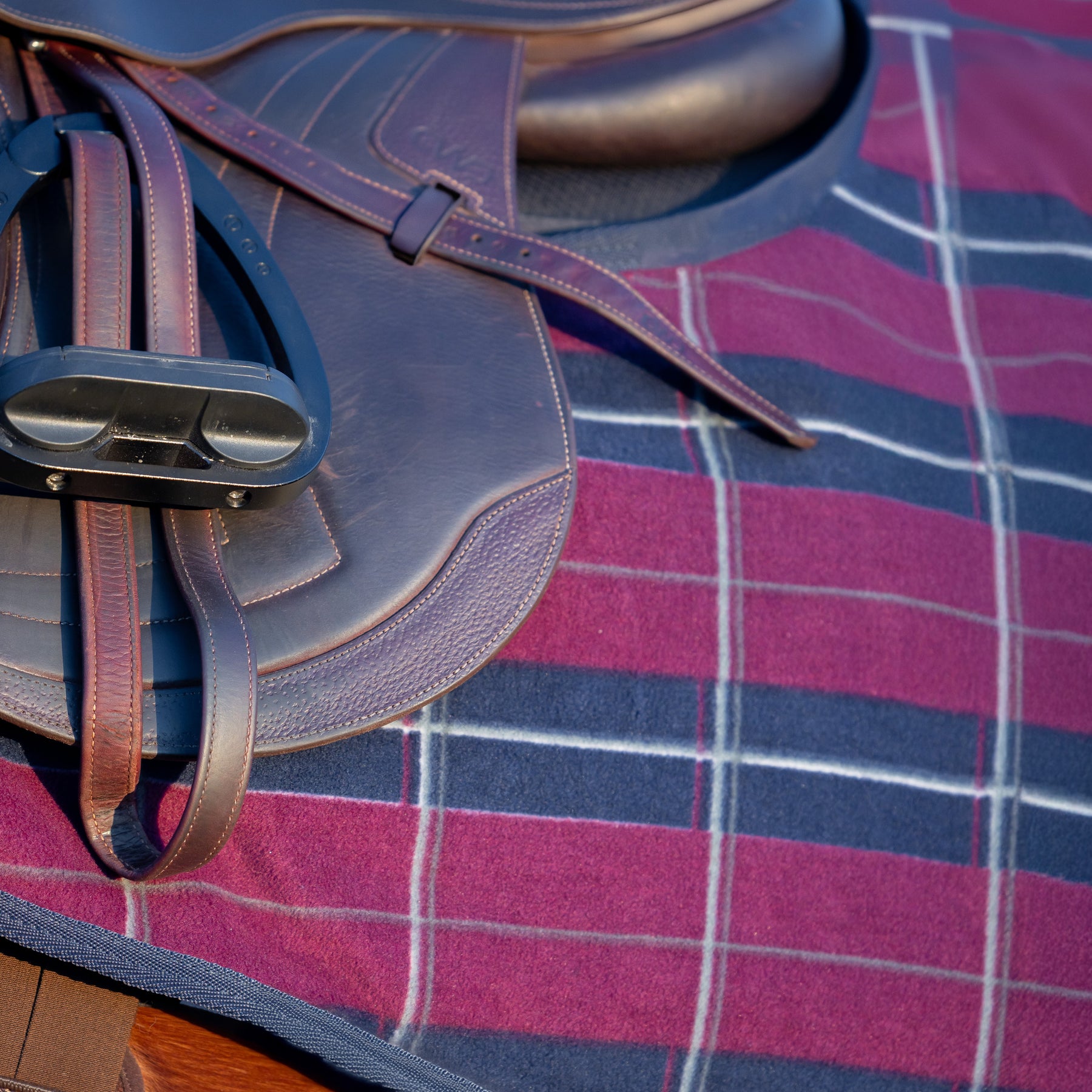Close-up side view of a bay horse wearing the Burgundy/Navy Equinavia Norse Fleece Quarter Sheet under a brown jump saddle