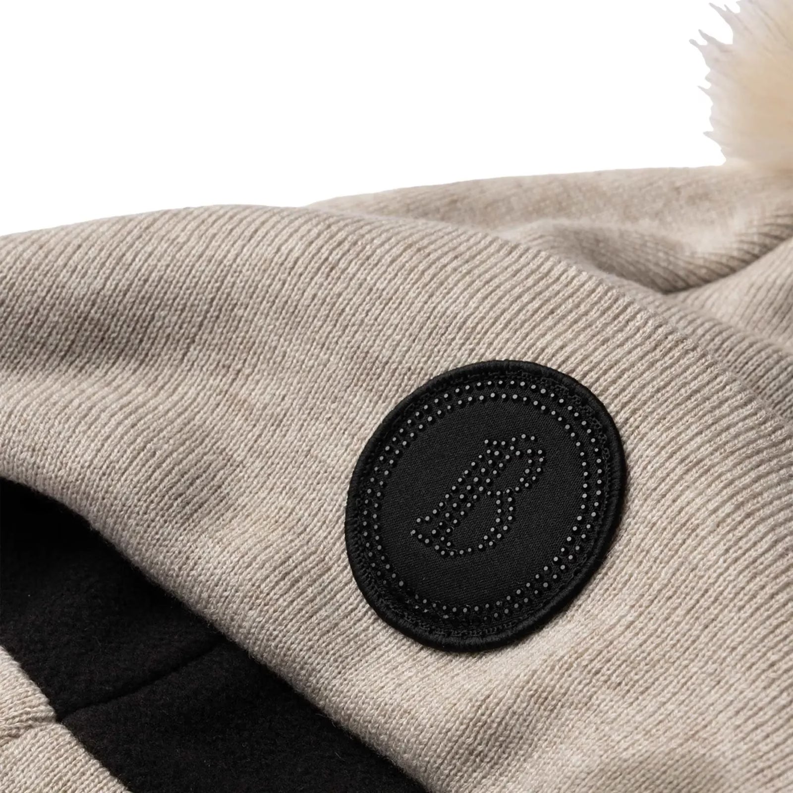 Close-up view of the "B" patch on the beige B Vertigo Sydney Knitted Hat on a white background