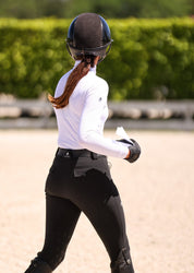 Back view of a female model wearing the Black Criniere Juliette High Compression Half Seat Breeches while walking in an outdoor arena