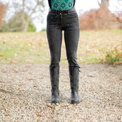 Front view of a model wearing the black Equinavia Dagny Leather Belt with black breeches and black boots while standing outside on a gravel path