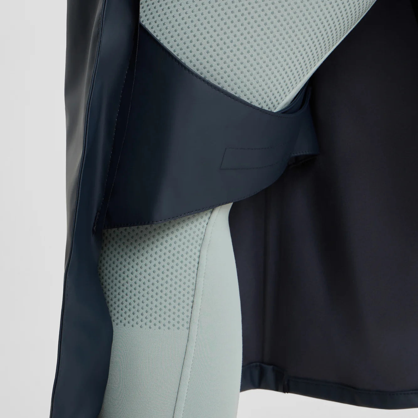 Side closeup view of a model wearing the Navy Horze Hazel Womens Long Raincoat on a plain background showing the leg straps inside