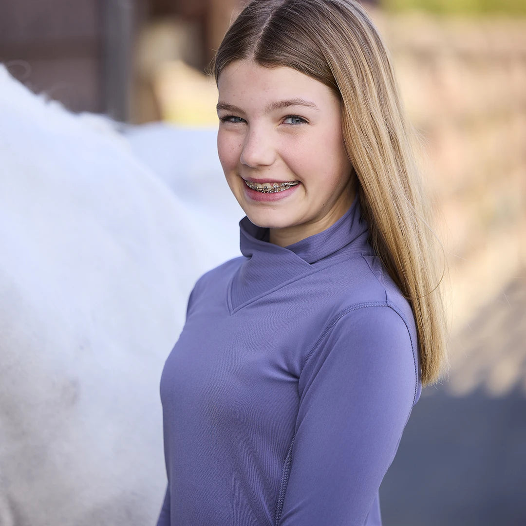 Light purple base layer top with mock neck shown on model with white pony in background