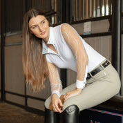 Angled front view of a female model wearing the White/Beach Blue Tredstep Ireland Monaco Air Long Sleeve Show Shirt while sitting on a tack box in a barn aisle