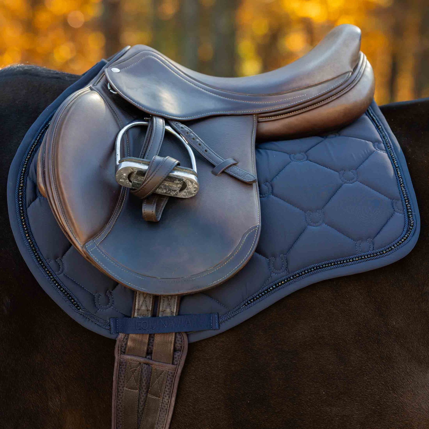 Side view of a horse wearing the Navy Equinavia Bergen Crystal All Purpose Pad under a brown saddle