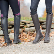 Back and front views of 2 female models wearing black and brown pairs of the Equinavia Josefine Winter Tall Riding Boots while standing on a gravel path outside