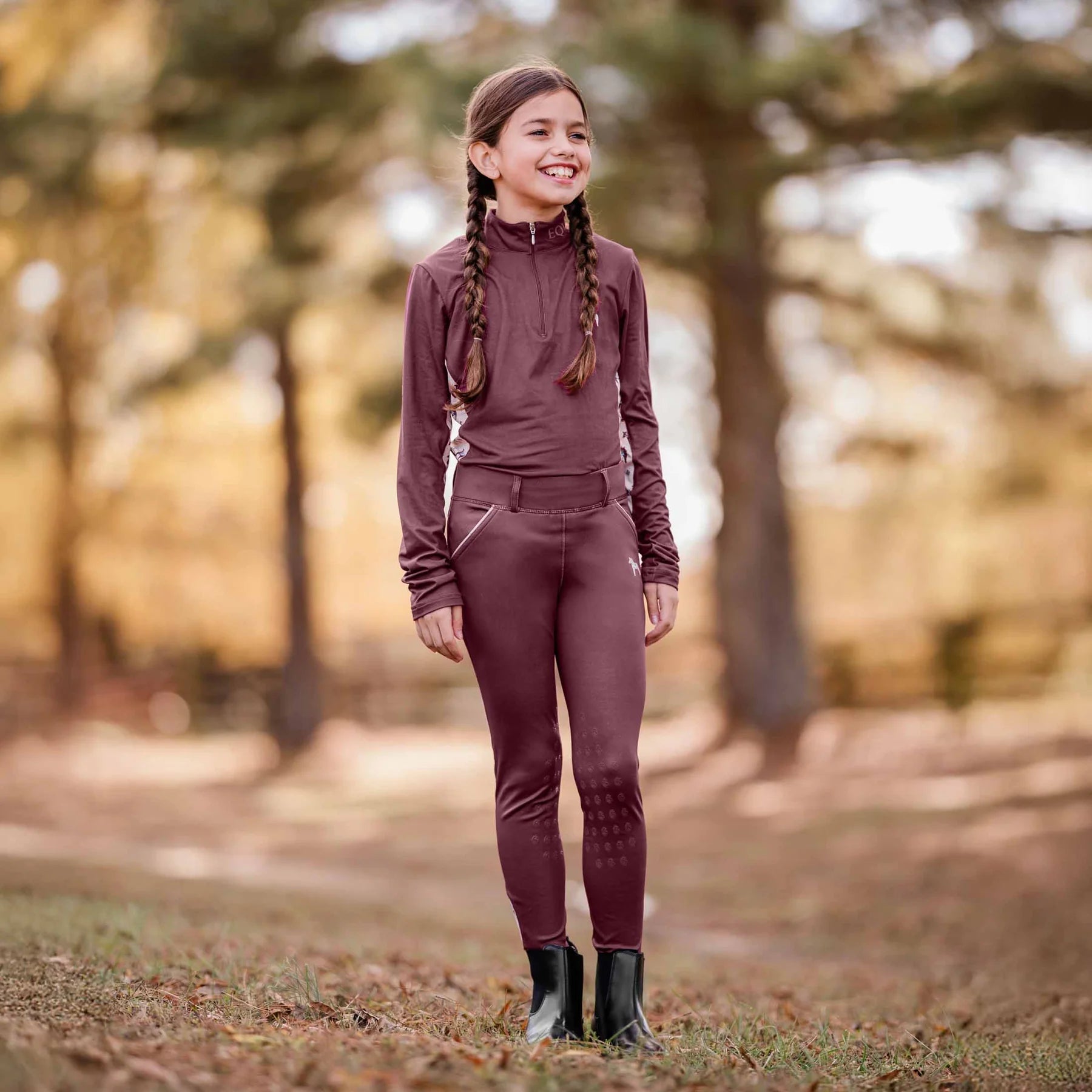 Front view of a young model wearing the Burgundy Equinavia Lena Kids Long Sleeve Quarter Zip outdoors