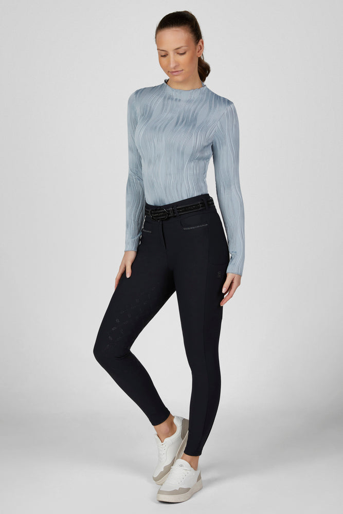 Full body front view of a female model wearing the Dusty Blue Pikeur Long Sleeve Waveline Shirt and navy breeches on a plain background
