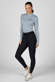 Full body front view of a female model wearing the Dusty Blue Pikeur Long Sleeve Waveline Shirt and navy breeches on a plain background