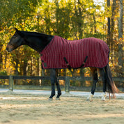 Side view of a dark colored horse wearing the Burgundy/Black Equinavia Luftig Waffle Cooler white standing in an outdoor arena