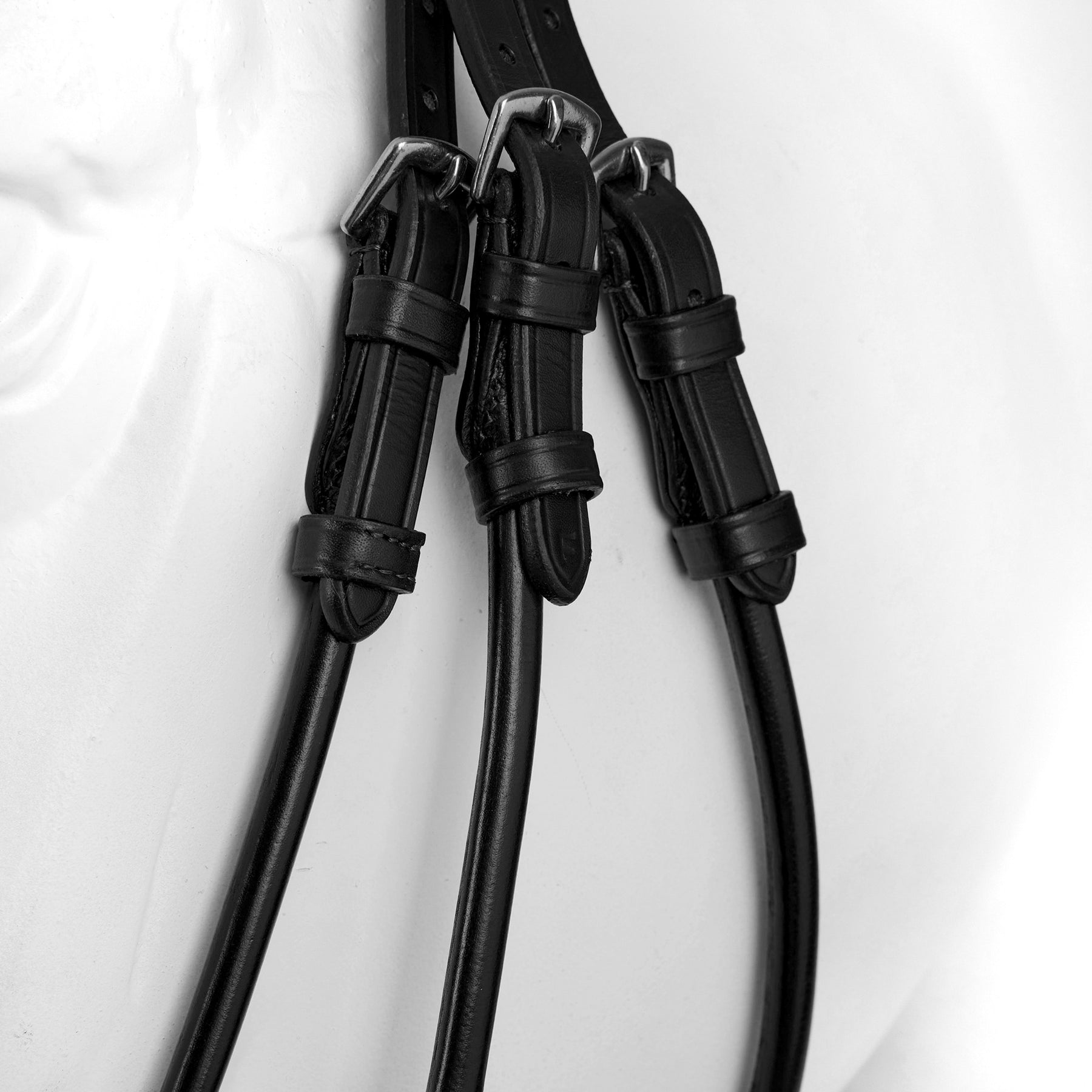Close-up view of the cheek of a white horse mannequin wearing the black Horze Montrose Dressage Bridle on a white background