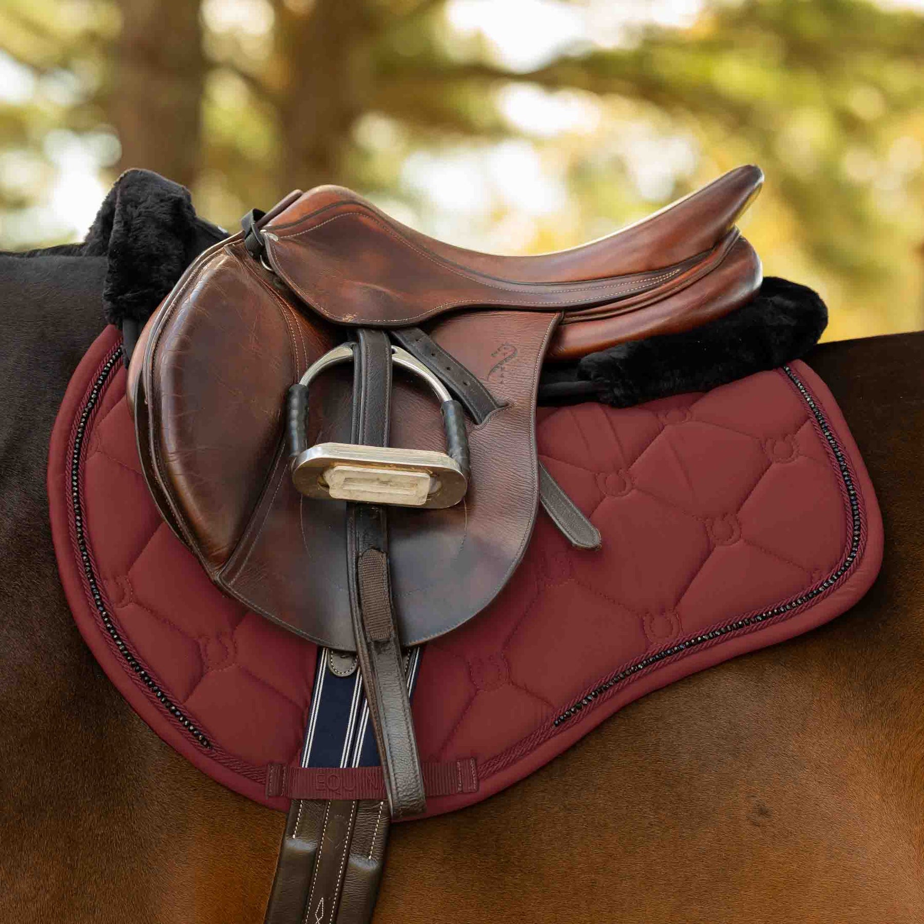 Side view of a horse wearing the Burgundy Equinavia Bergen Crystal All Purpose Pad under a brown saddle