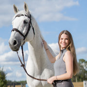 Side view of a female model wearing the Volcanic Glass Tredstep Ireland LA Sport Sleeveless Training Shirt while standing next to a gray horse outside