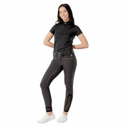 Full body front view of a model wearing the black Equinavia Kari Short Sleeve Sun Shirt With NordicAir Tech, dark breeches, and white shoes on a white background