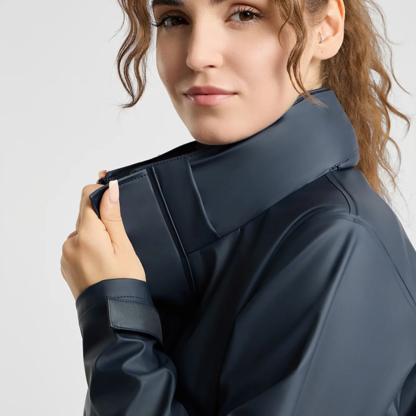 Side closeup view of a model wearing the Navy Horze Hazel Womens Long Raincoat on a plain background showing the shoulder, adjustable cuffs, and collar