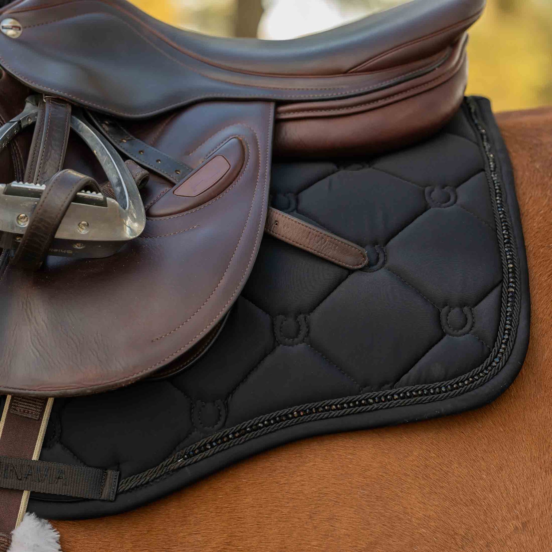 Close-up side view of the Black Equinavia Bergen Crystal All Purpose Pad under a brown saddle