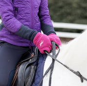 Close-up view of a model wearing the Deep Coral Pink Horze Kids Fleece Gloves while riding a white horse