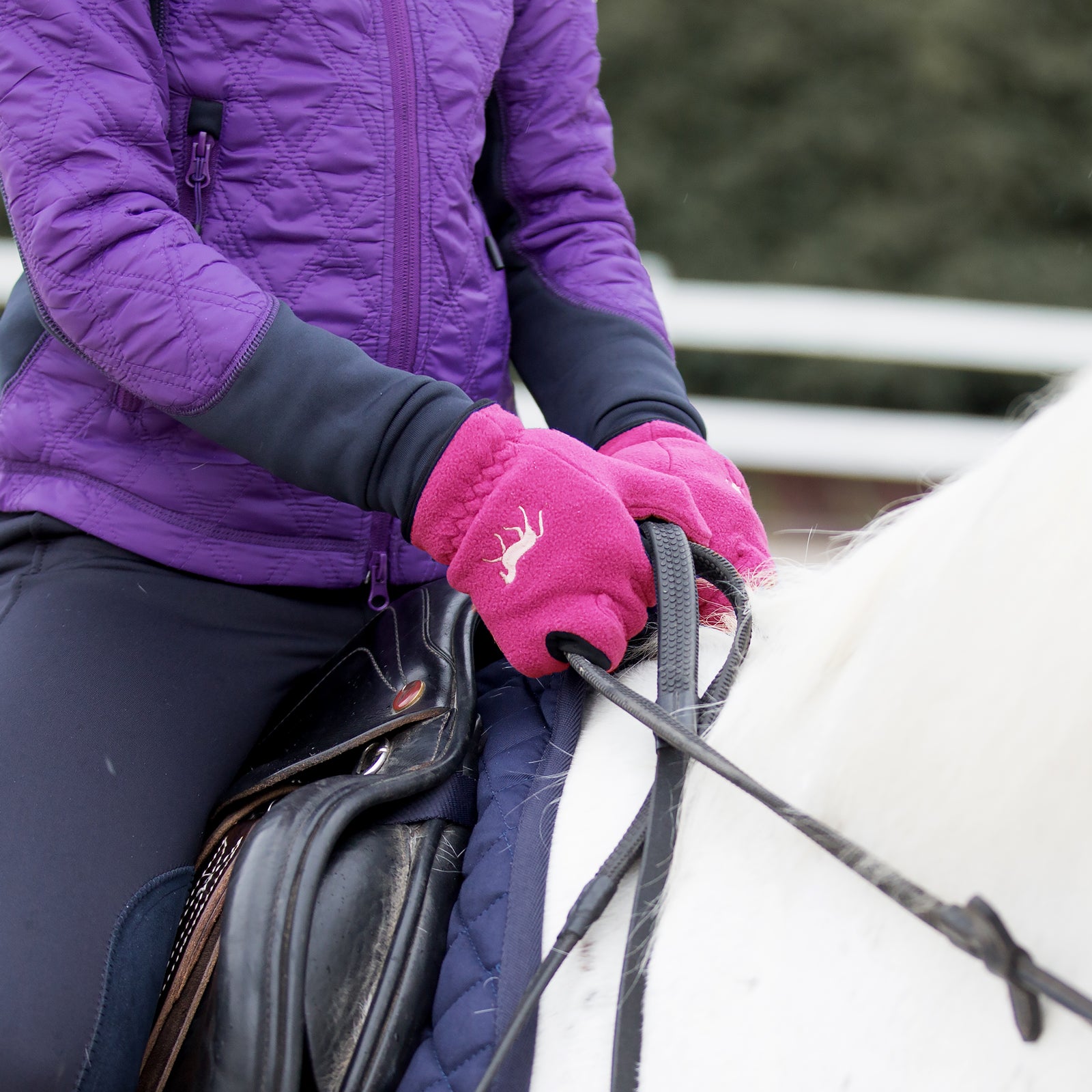 Close-up view of a model wearing the Deep Coral Pink Horze Kids Fleece Gloves while riding a white horse