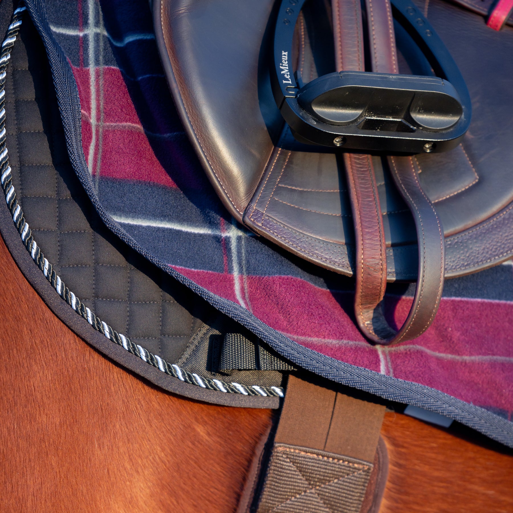 Close-up side view of a bay horse wearing the Burgundy/Navy Equinavia Norse Fleece Quarter Sheet under a brown jump saddle